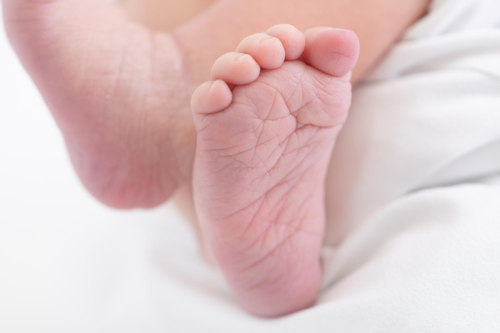 Close-up of a baby’s bare foot resting on a white blanket, showing the toes and soft, wrinkled sole in gentle, natural light.
