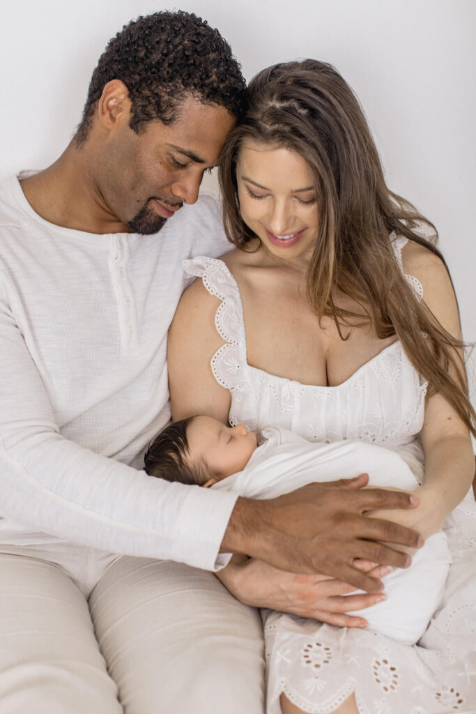 A couple wearing white holds their newborn baby in a photography studio in Newport Beach.