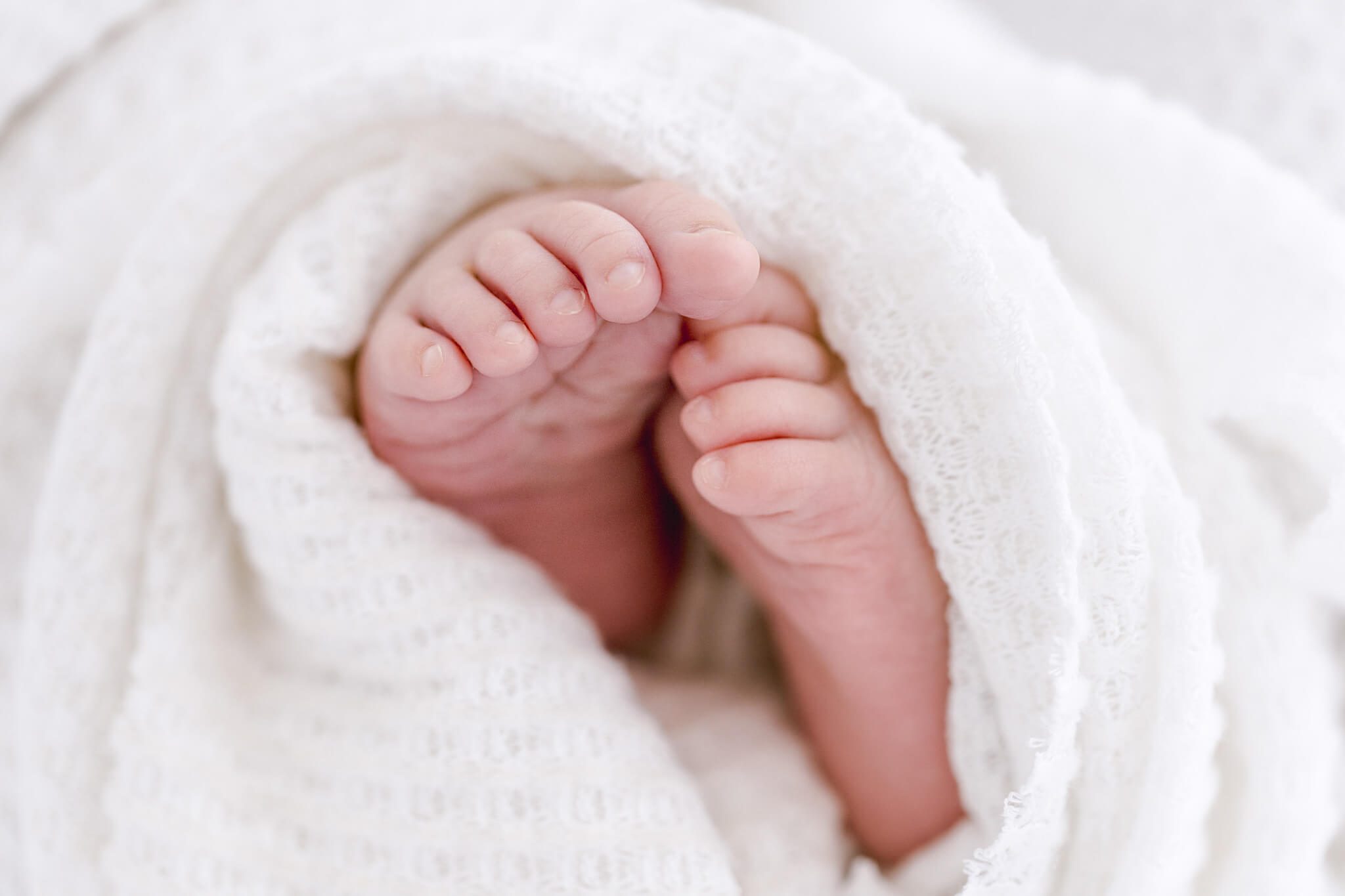 Tiny newborn baby toes peeking out from a soft white knit blanket during a newborn photography session.