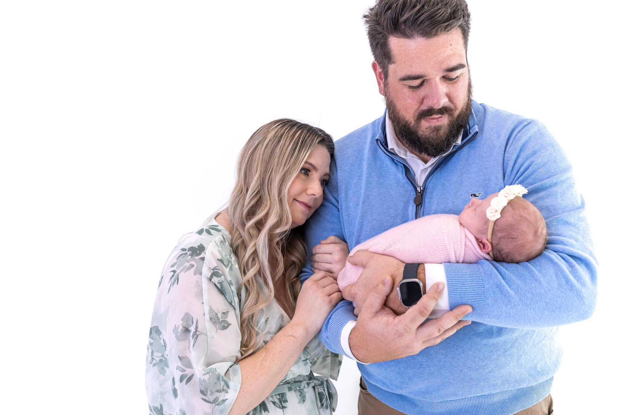 dad standing and holding his new baby while mom holds on top his arms and looks in with a peaceful expression