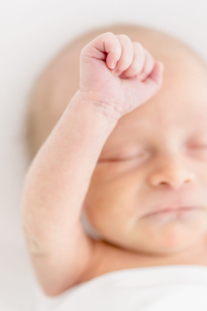A close-up of a sleeping newborn baby with eyes closed and one arm raised at a newborn shoot at Jennifer Imus Photography's studio in Orange County.