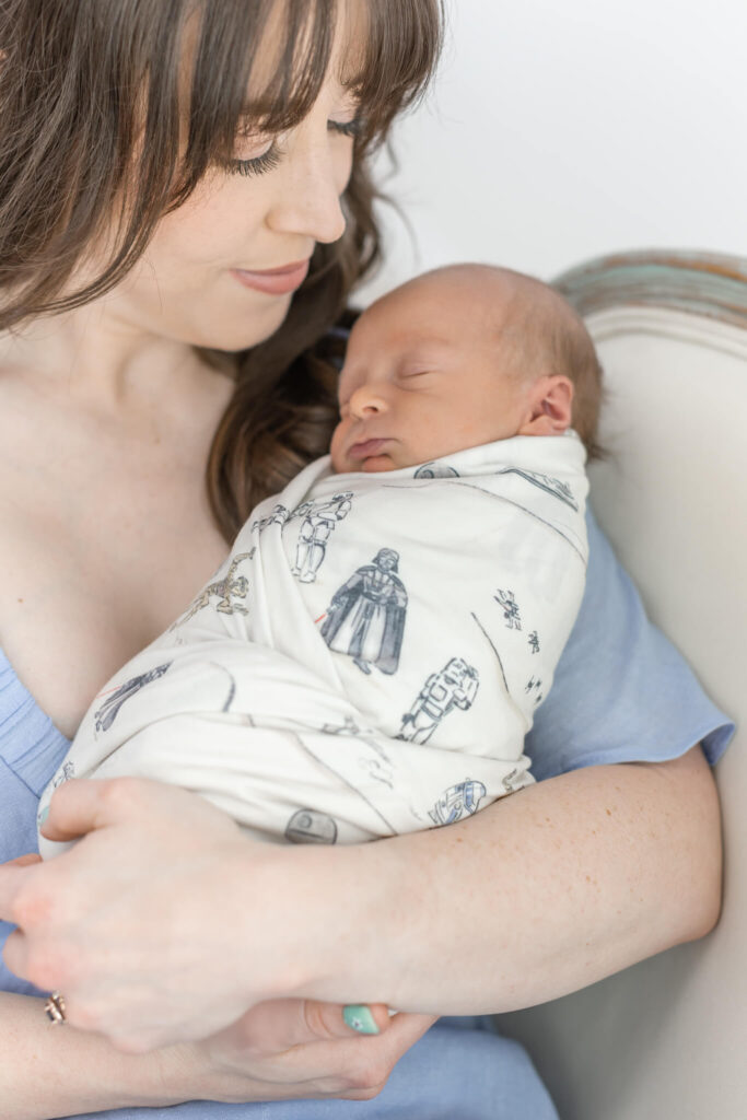 A woman in blue cradles a sleeping newborn wrapped in a Star Wars blanket.