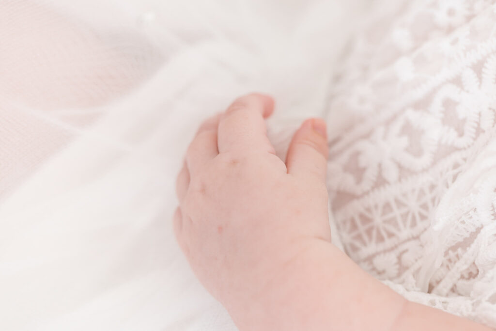 A close-up of a newborn baby's hand gently resting on a white fabric in Orange County.