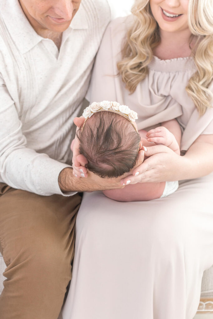 A man and woman dressed in light colors, cradle a newborn baby during an Orange County newborn photoshoot.