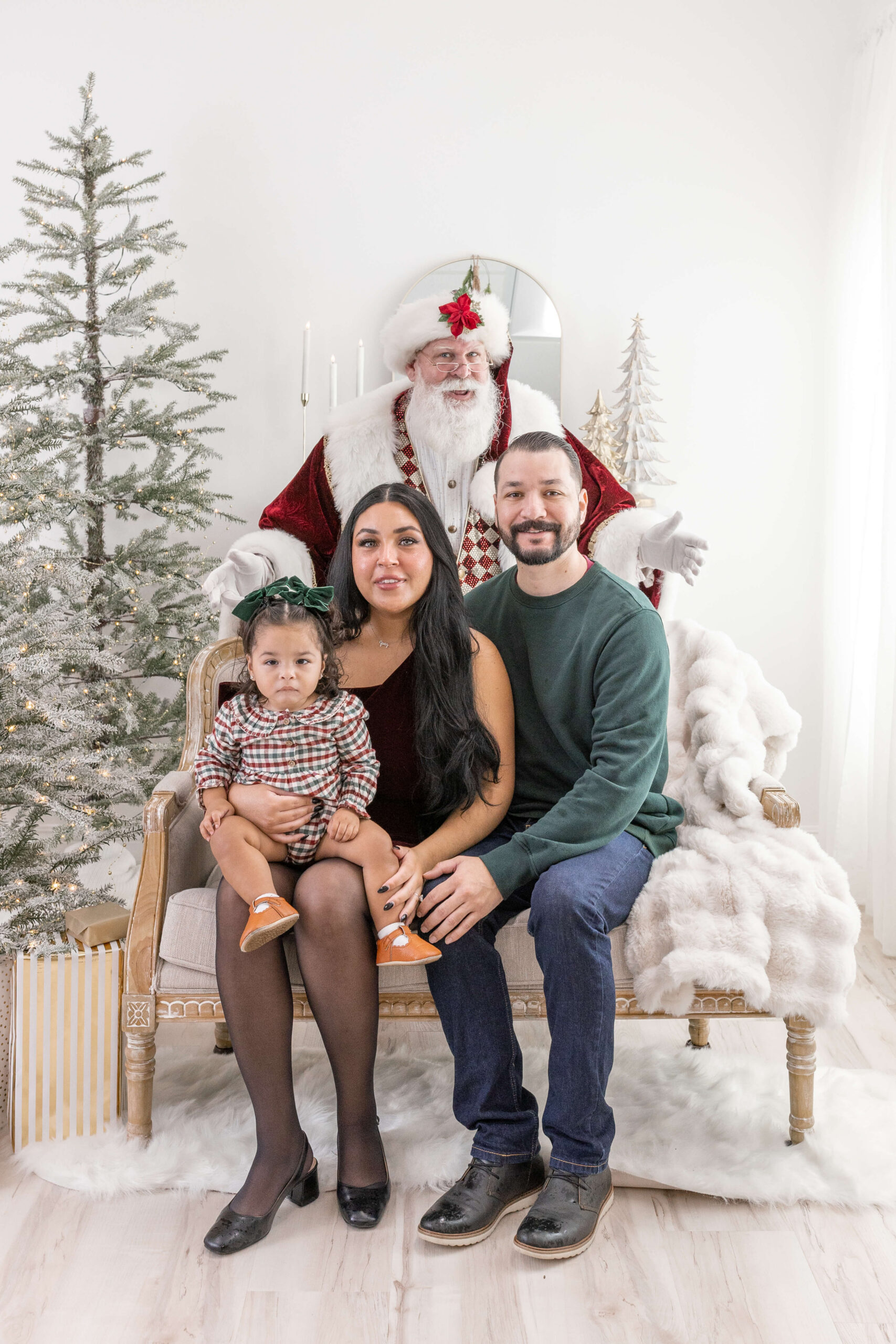 Family of 3 sitting on a couch with Santa behind them