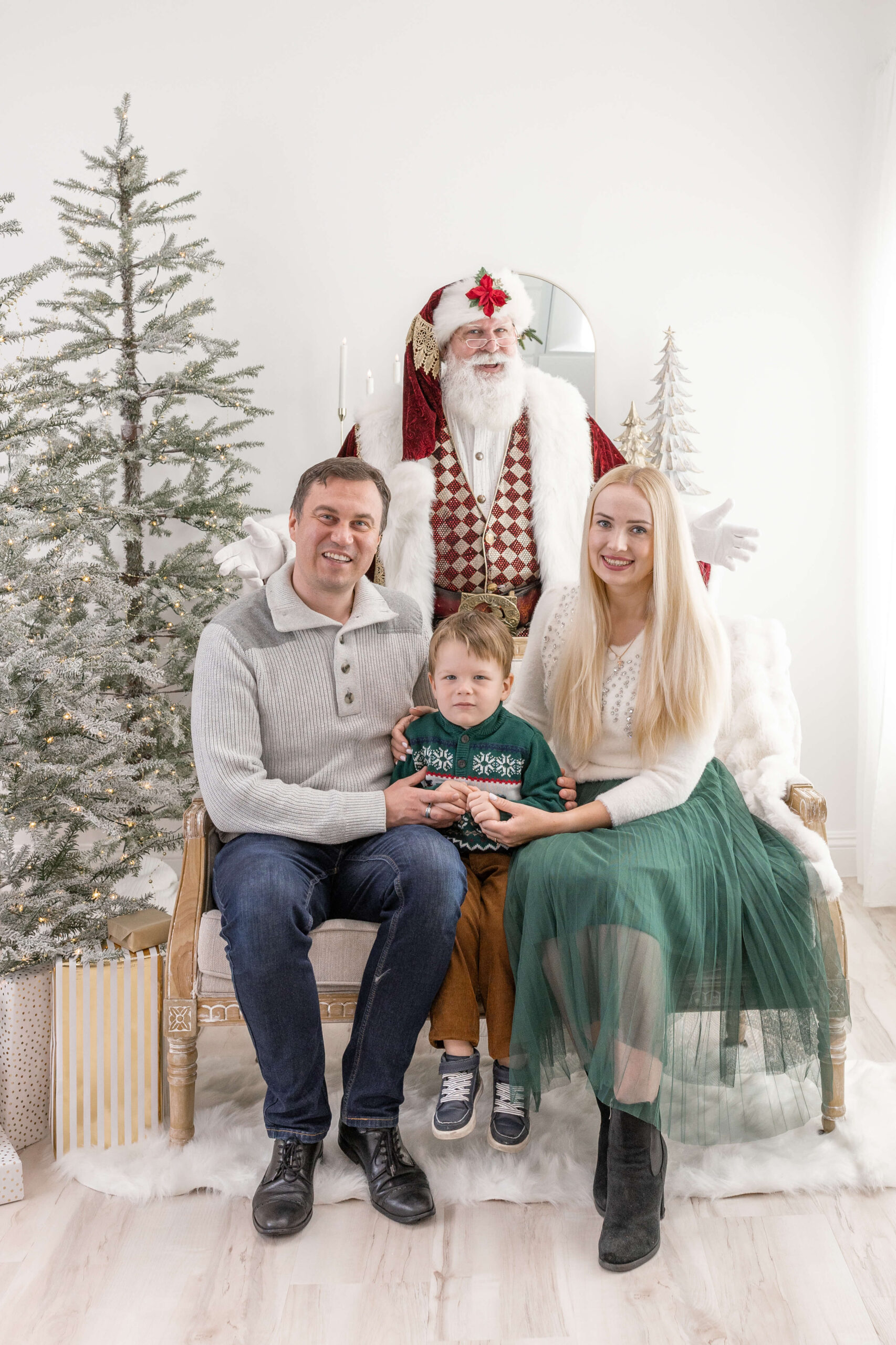 A family of 3 sitting on a couch with Santa behind them