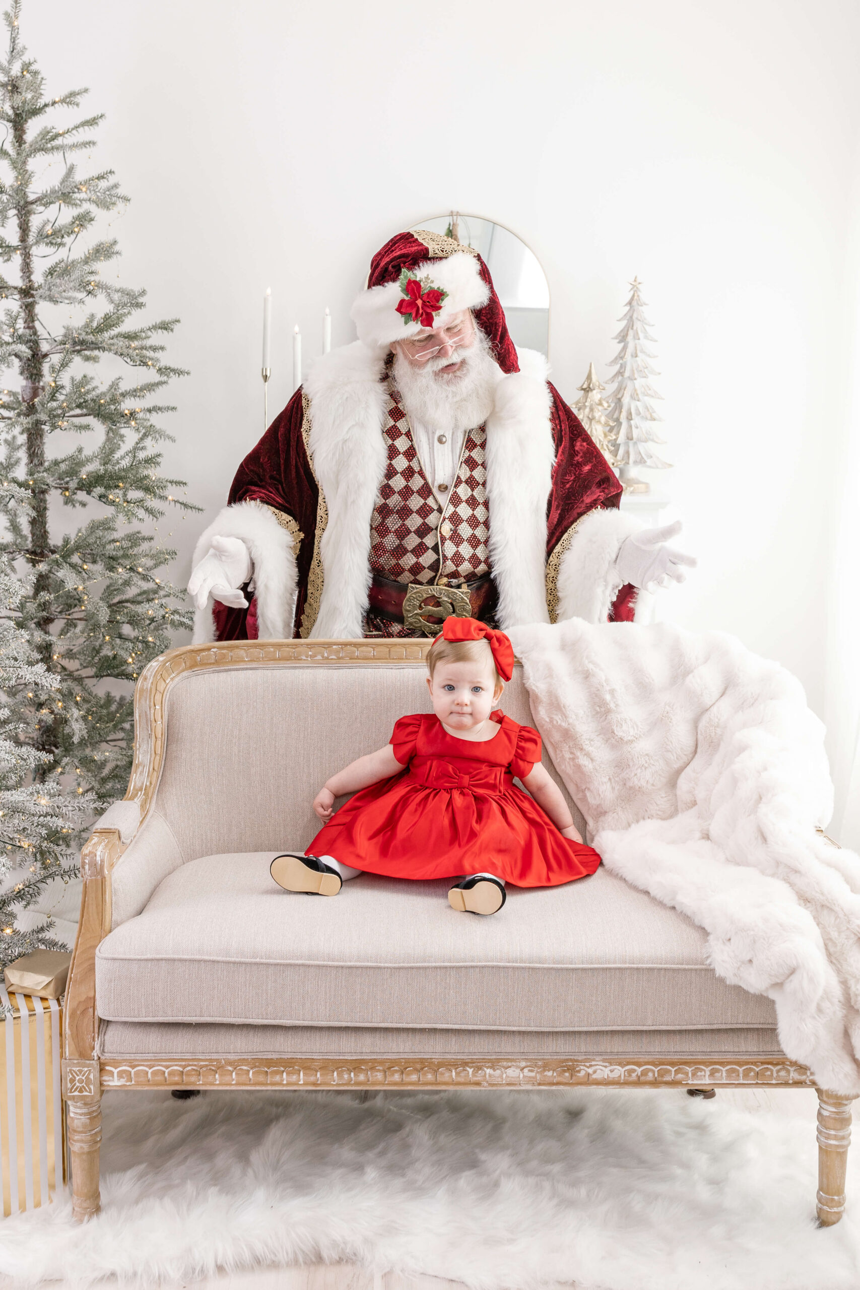 Girl in a red dress on a couch with Santa behind her