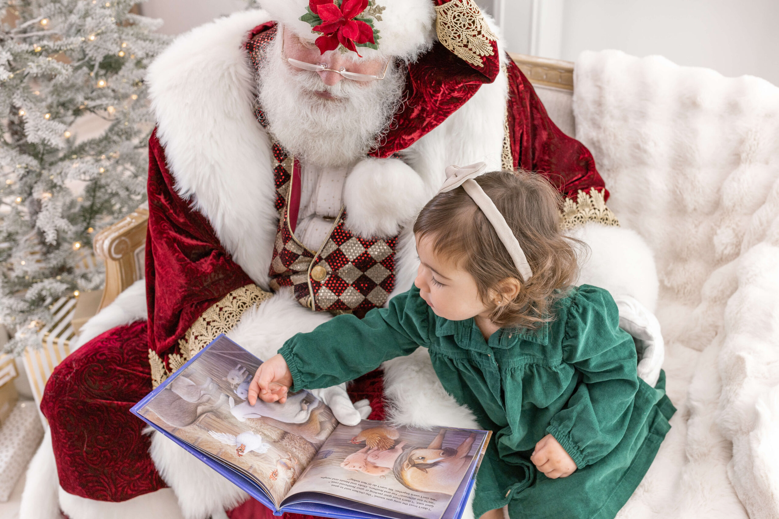 A little girl in a green dress reading a book with Santa